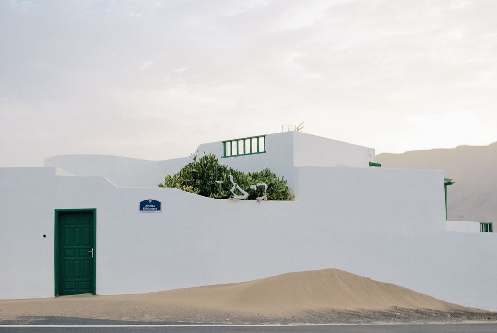 White building with a green door amidst a desert landscape, featuring clear sky and greenery.